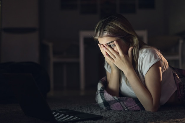 Young beautiful woman at night watching a movie on a laptop