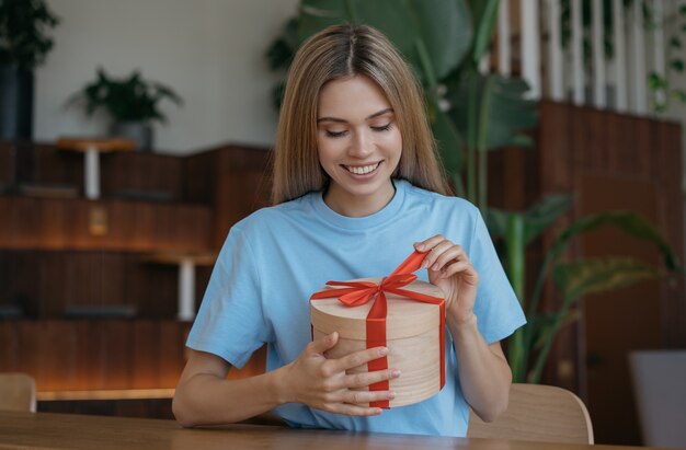 Фото Молодая красивая женщина открывает подарочную коробку дома
