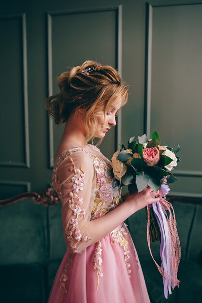 Young beautiful woman in a pink dress standing in a vintage room