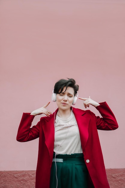 ピンクのヘッドフォンをかぶった美しい若い女性がピンクの壁の背景で音楽を聴いています