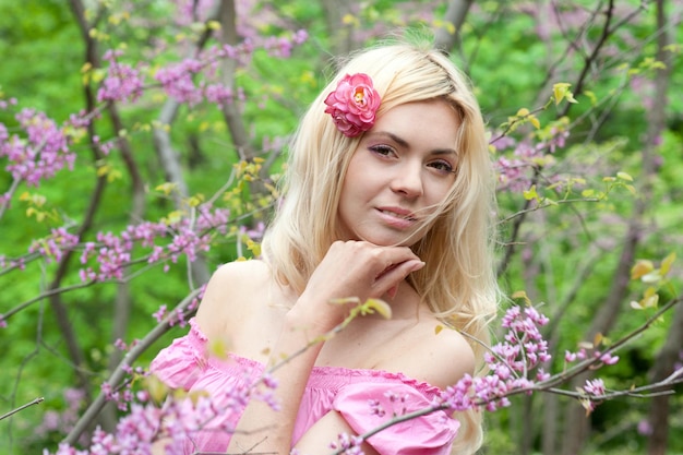 Young beautiful woman posing in blooming pink flowers spring park