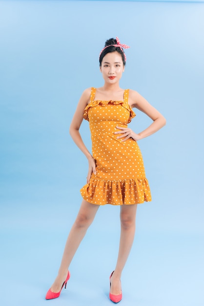 Young beautiful woman posing in new casual yellow and white dotted dress on a blue