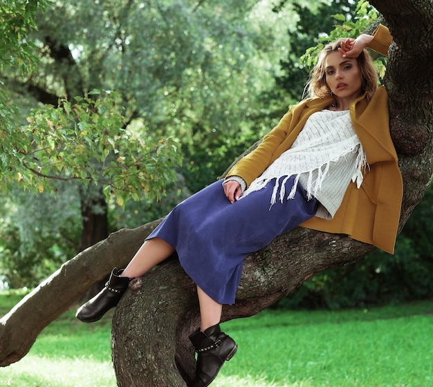 Giovane bella donna in posa su un albero. ritratto di moda glamour. parco d'autunno.