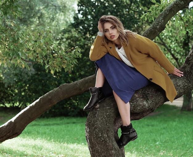 Young beautiful woman posing on a tree Glamour fashion portrait Autumn park