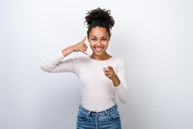 Young beautiful woman posing over white isolated background smiling and doing talking on the telephone gesture while pointing to you Call me concept