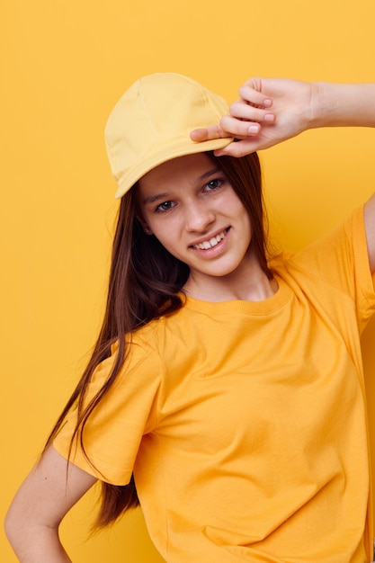 黄色のTシャツとキャップの黄色の背景でポーズをとって若い美しい女性