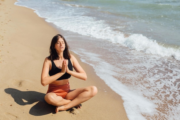 Young beautiful woman practicing yoga on the beach sitting on sand and meditaning mental health and self care concept happy girl relaxing on seashore on summer vacationxa