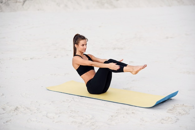 Young beautiful woman practicing yoga, doing press ups exercise on the beach of the sea. Fitness yoga and healthy lifestyle concept. Beautiful woman in sports wear doing exercise on yoga mat.