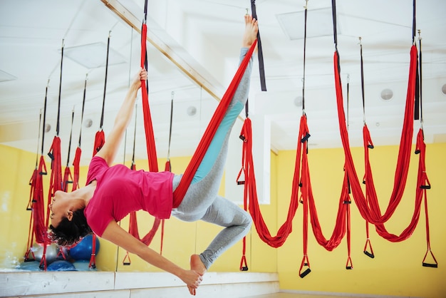 Mosca di pratica di yoga della giovane bella donna con un'amaca in studio.