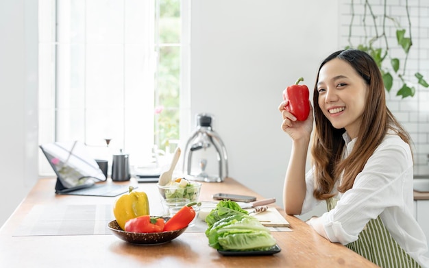 若くてきれいな女性がキッチン ルームで新鮮な野菜や果物から健康食品を調理を準備します笑顔とカメラ目線