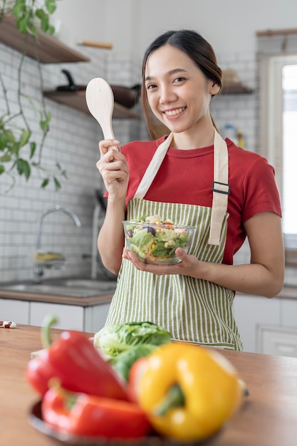 Young beautiful woman prepares cooking healthy food from fresh vegetables and fruits in kitchen room Smiling and looking at camera