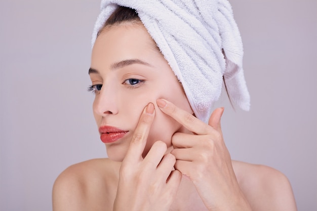 The young beautiful woman presses acne on a cheek.