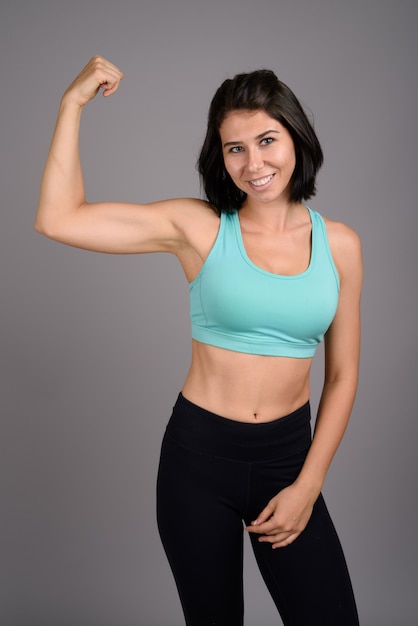 Young beautiful woman ready for gym against gray background