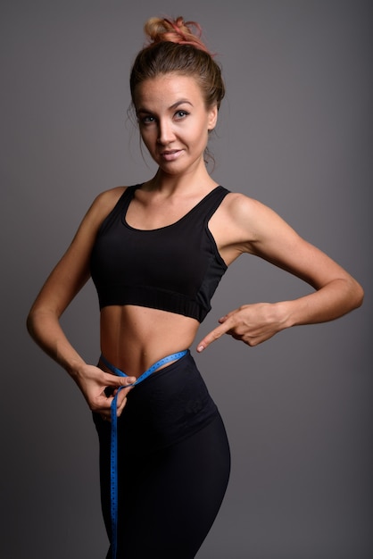 young beautiful woman ready for gym against gray wall