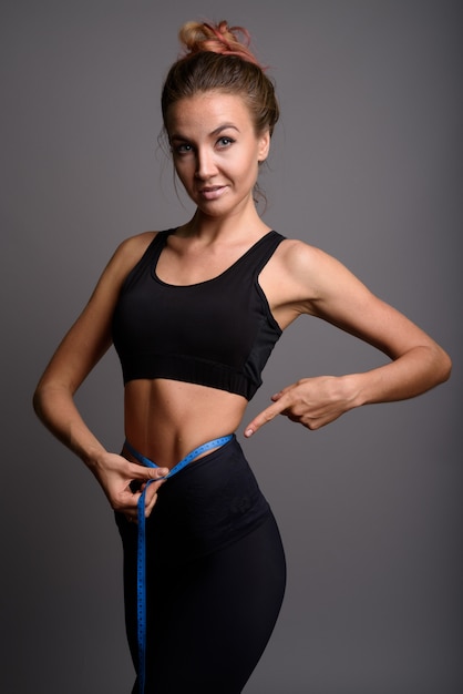 Young beautiful woman ready for gym against gray wall