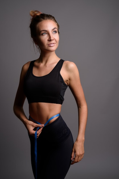 Young beautiful woman ready for gym against gray wall