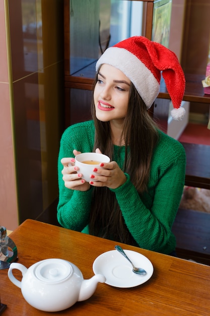 Young beautiful woman in red Santas hat drinking tea in cafe