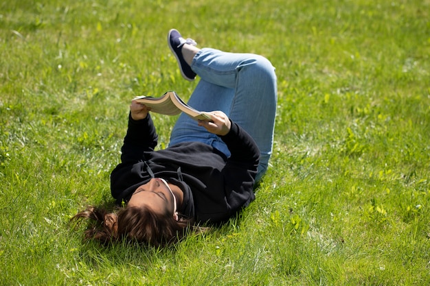 Фото Молодая красивая женщина расслабляется в чтении природы, лежа на зеленой траве