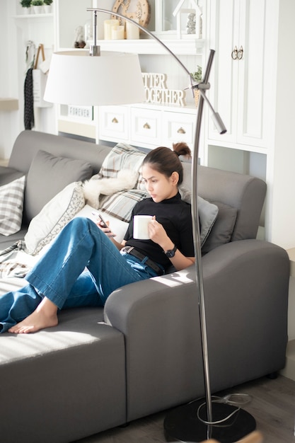 Young beautiful woman relaxing on sofa at home and using smart phone