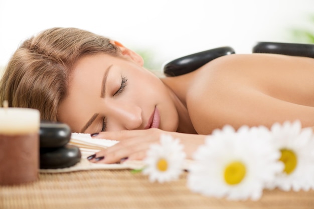 Young beautiful woman relaxing at spa centre. She is enjoying at stone massage.