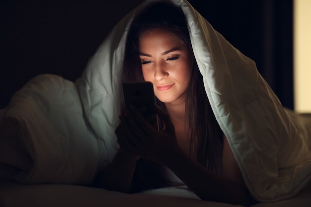 young beautiful woman resting in bed with smartphone