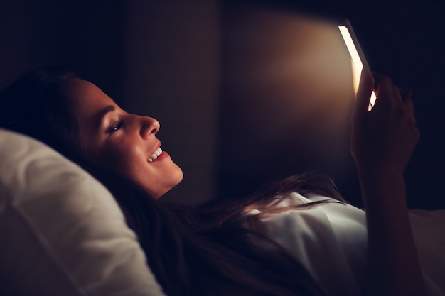 young beautiful woman resting in bed with smartphone