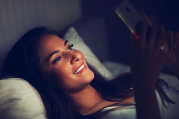Giovane bella donna che riposa a letto con smartphone