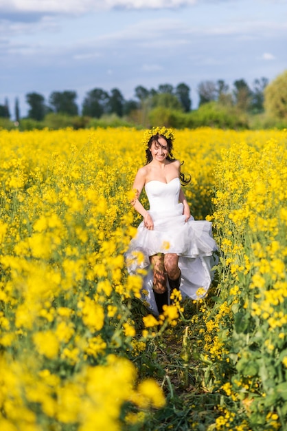 Young beautiful woman runs through a field with yellow flowers The bride in a long white dress and boots in a rapeseed field