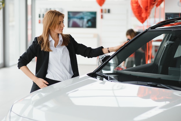 Foto giovane bella donna che mostra il suo amore per un'auto in uno showroom di auto