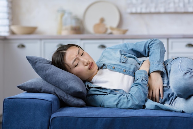 Young beautiful woman sick alone at home lying on bed asian\
girl holding hands on stomach having