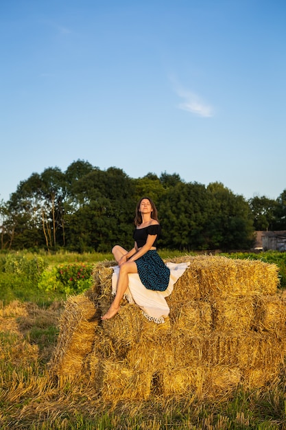 Young beautiful woman sits on a large pile of straw bales