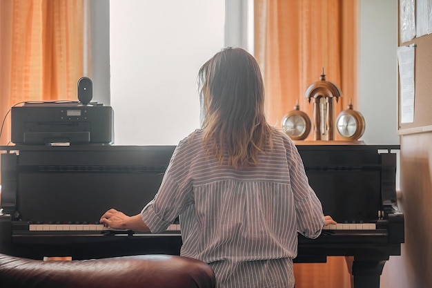 A young beautiful woman sits with her back to us and plays the
piano, music lessons in young people