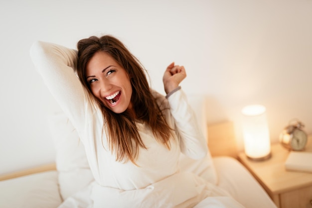 Photo young beautiful woman sitting in the bed in morning and stretching.