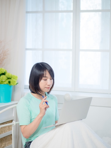 Young beautiful woman sitting in bedroom and using laptop in the morning