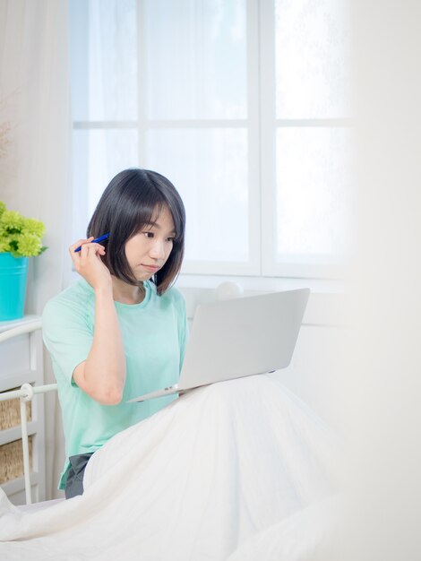 Young beautiful woman sitting in bedroom and using laptop in the morning