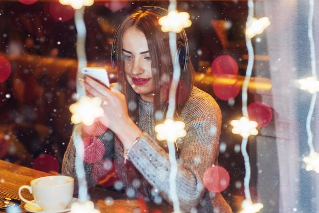 Giovane bella donna che si siede nella caffetteria, bere caffè. modella l'ascolto di musica. natale, felice anno nuovo, san valentino, vacanze invernali