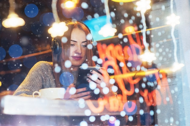 Young beautiful woman sitting in cafe, drinking coffee. Model listening to music. 