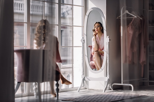 Young beautiful woman sitting near windows looking to mirror