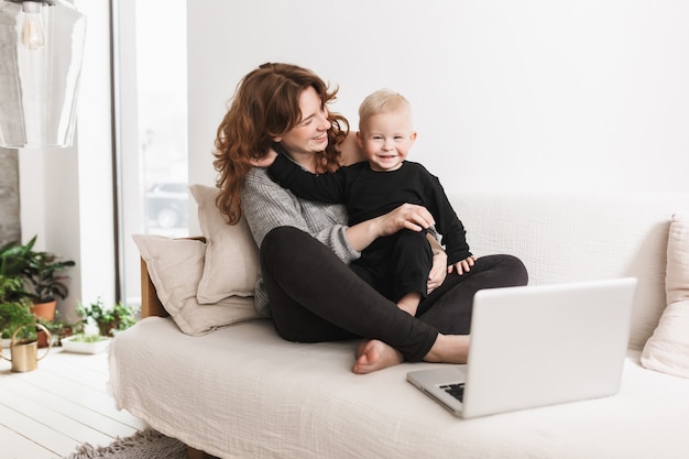 写真 幸せに彼女の小さな笑顔の息子と一緒にソファに座っている若い美しい女性