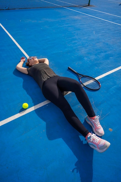 Young beautiful woman sitting at tennis cort after doing fitness exercise Girl rest after workout outdoors