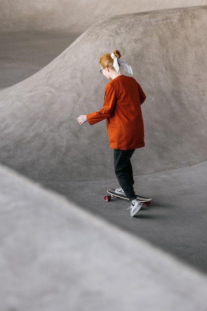 A young and beautiful woman skater a woman in an orange jacket rides a skateboard on a skate pad