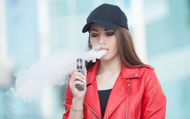 Young beautiful woman smoking ( vaping ) e-cigarette with smoke