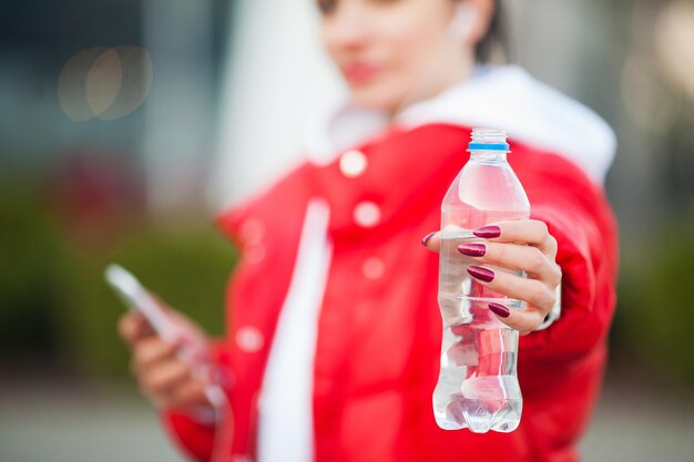 都市に立ち向かいながらスポーツドリンクを飲むスポーツウェアの若い美しい女性