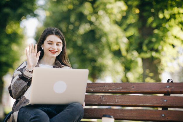 Giovane bella donna in piedi su una panchina utilizzando il computer portatile