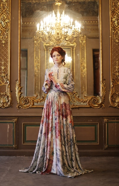 Young beautiful woman standing in the palace room with mirror.