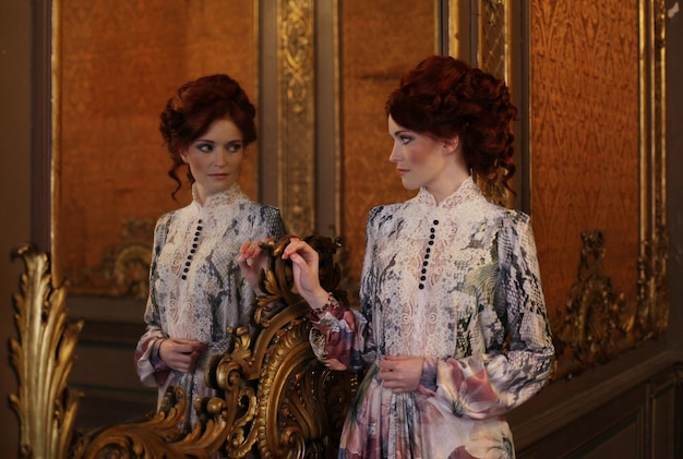 Young beautiful woman standing in the palace room with mirror