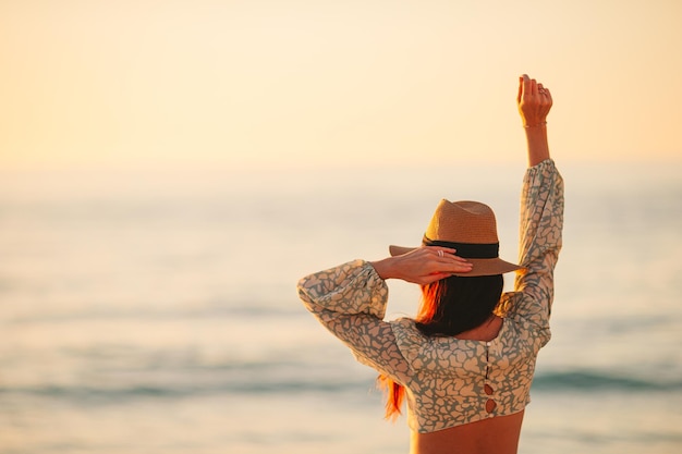 Giovane bella donna al cappello di paglia sulla spiaggia al tramonto