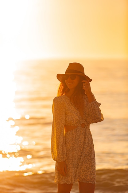 Foto giovane bella donna al cappello di paglia sulla spiaggia al tramonto