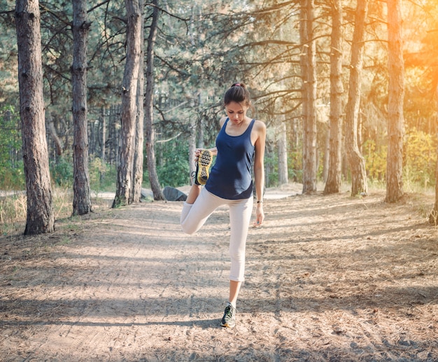 Giovane bella donna che allunga nella foresta di autunno al tramonto