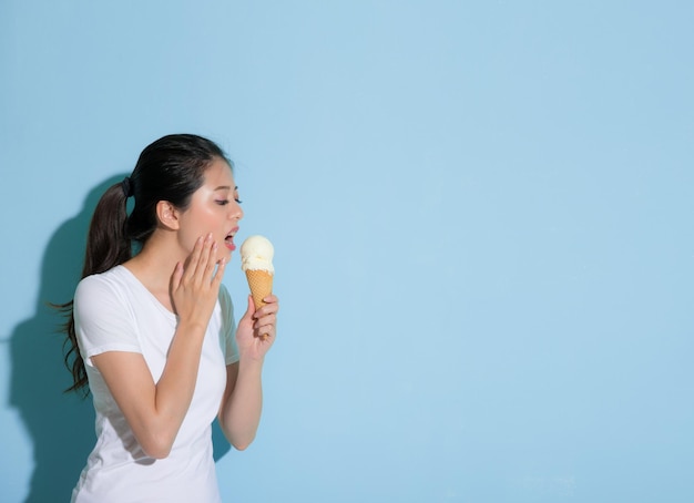 young beautiful woman suffering sensitive tooth disease challenge to eat ice cream and hand holding pain site worried about injury uncomfortable on blue background.